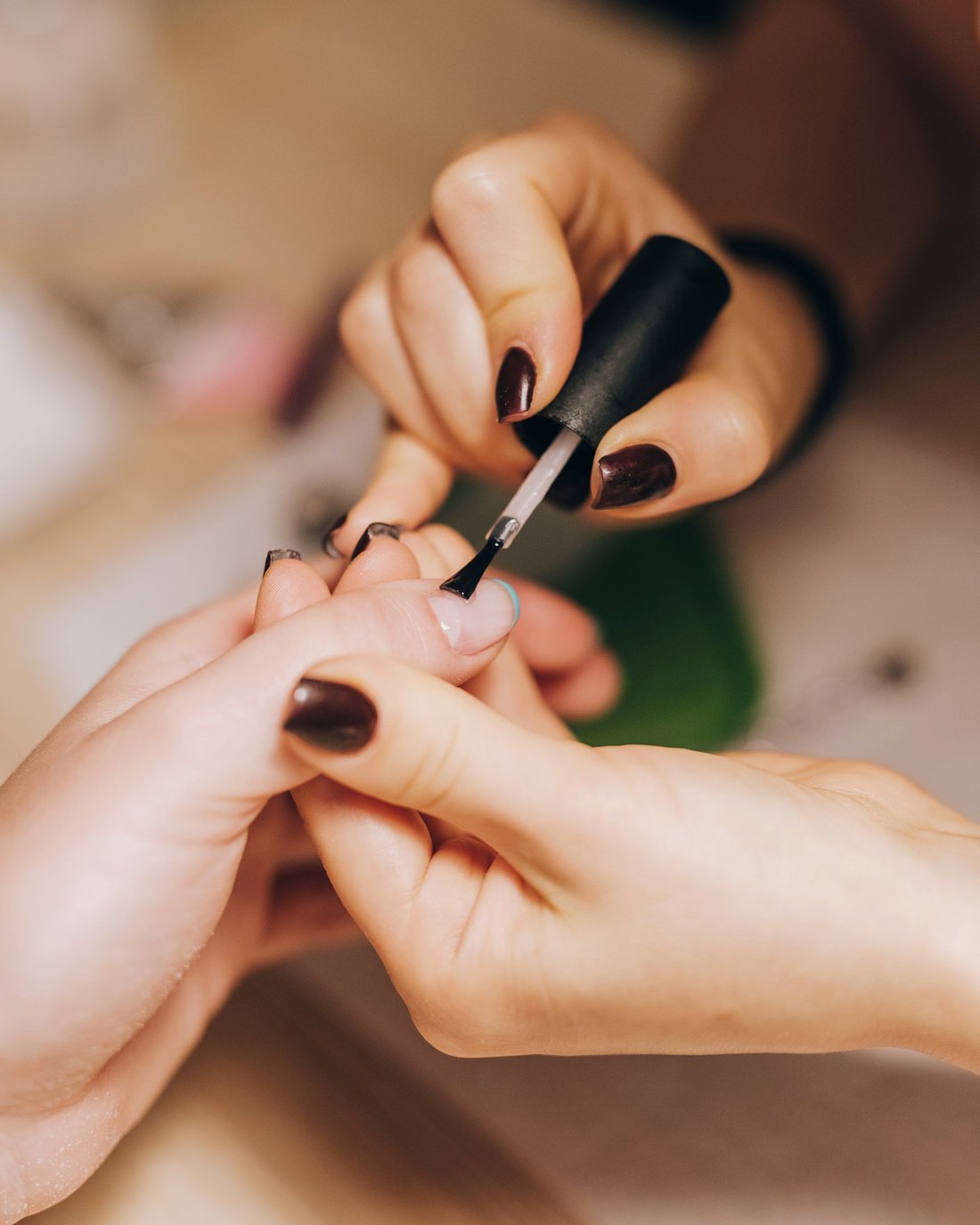 A nail artist applying dark polish